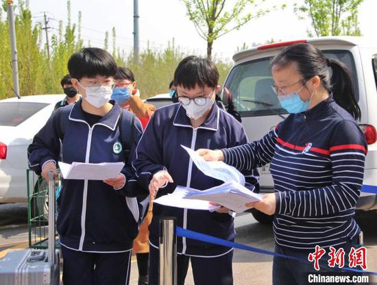 图为返校学生在校门口向老师交健康登记卡和山东省健康通行码。　赵晓